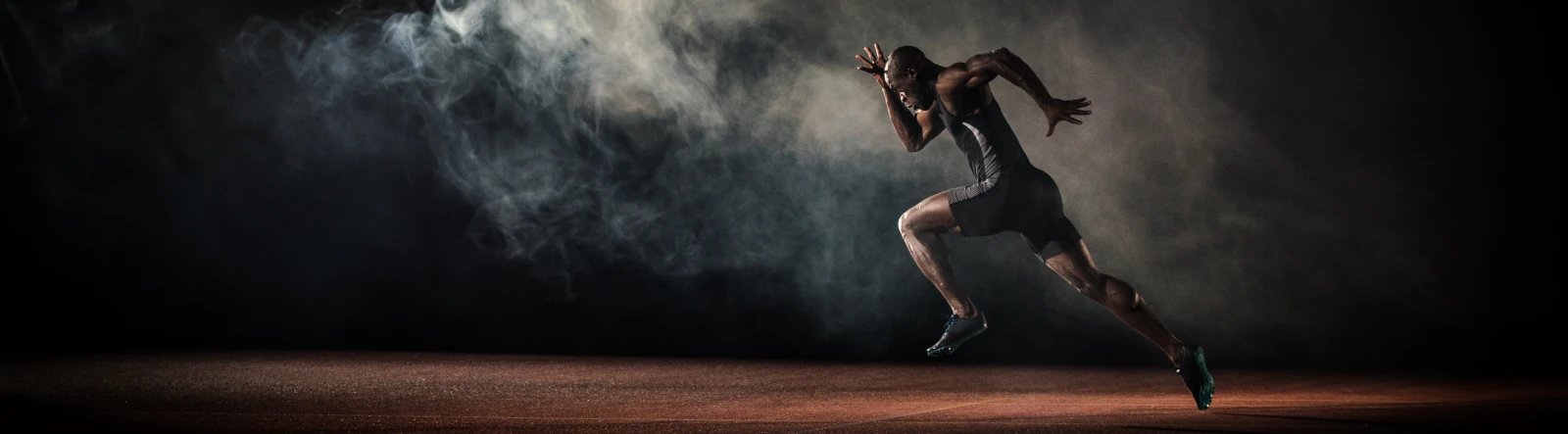 a sprinter running on a track in the dark through lit smoke
