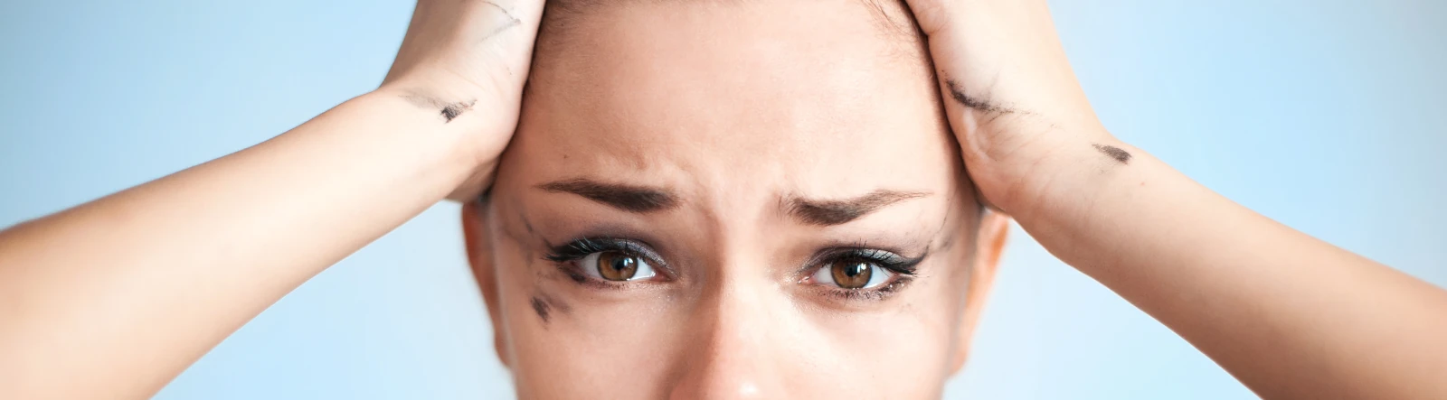 a stressed woman with smudged mascara and hands on her head