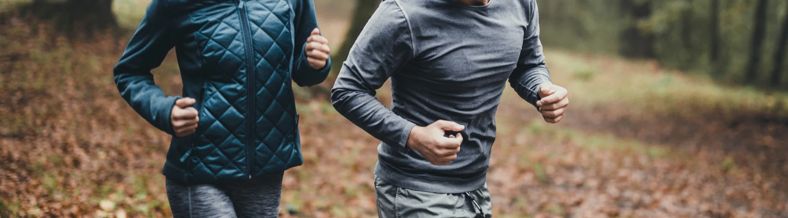 The torsos of two people running in the woods