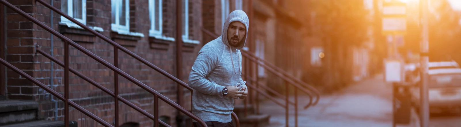 A man in an exercise hoody walking down stairs outside his home at dawn