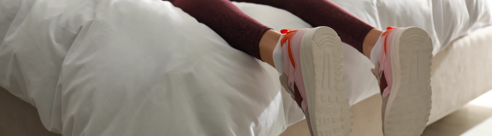 The lower legs of a woman lying on a bed wearing sneakers