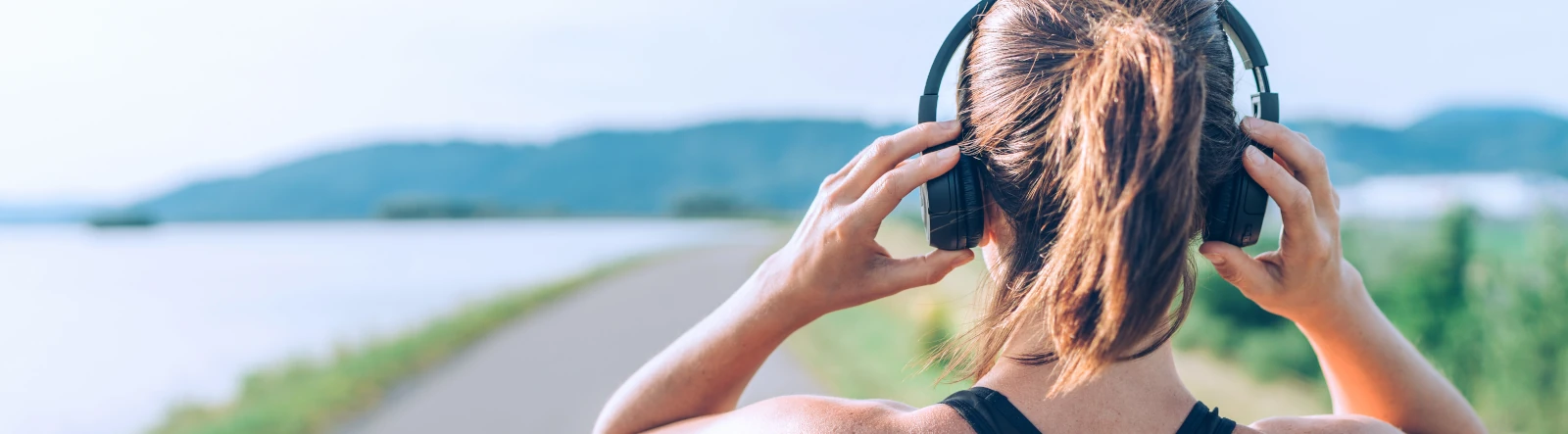 A view from behind of a woman wearing headphones and looking into the distance