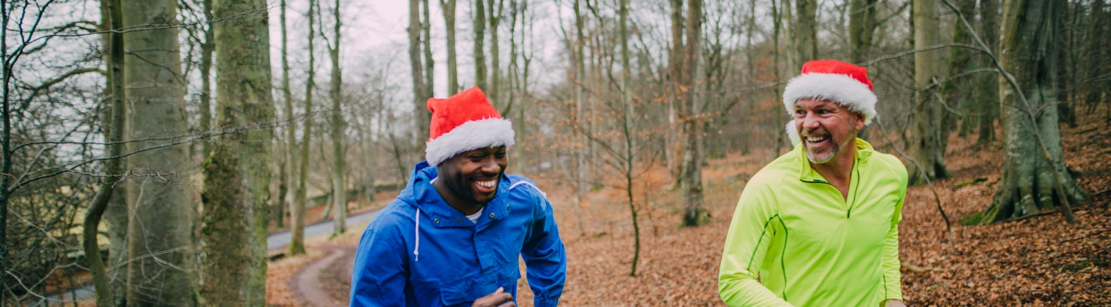 Two happy men running on a trail path while wearing santa hats