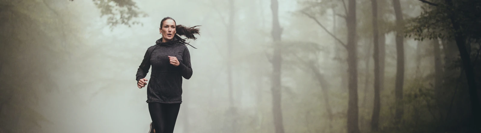 A woman running through a forest in the morning mist