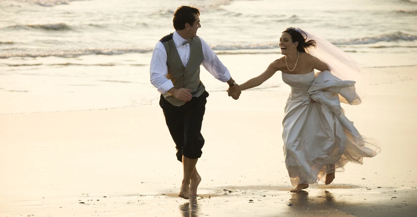 A bride and groom running on the beach