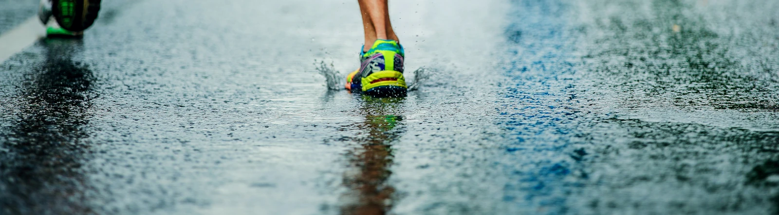 A runner's shoe landing on wet tarmac and making a small splash