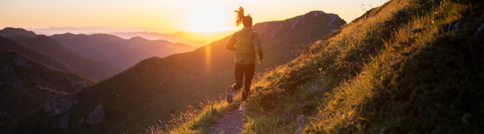 A woman running over hilly terrain in the sunset