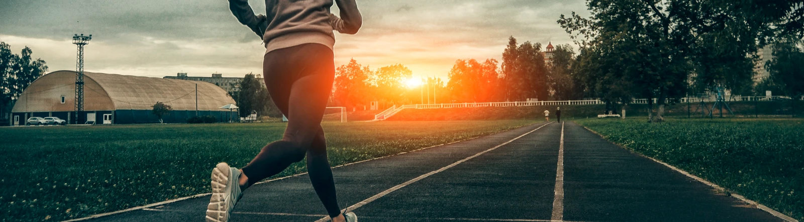 A woman running on a track with the sun rising or setting in the background