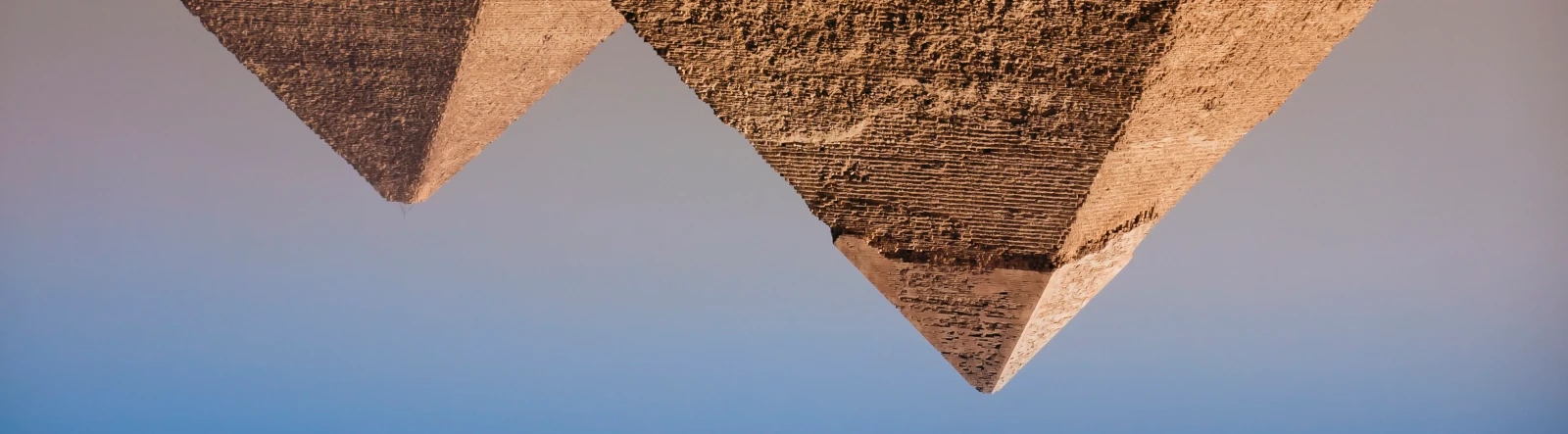 Two pyramids inverted with blue sky in the background